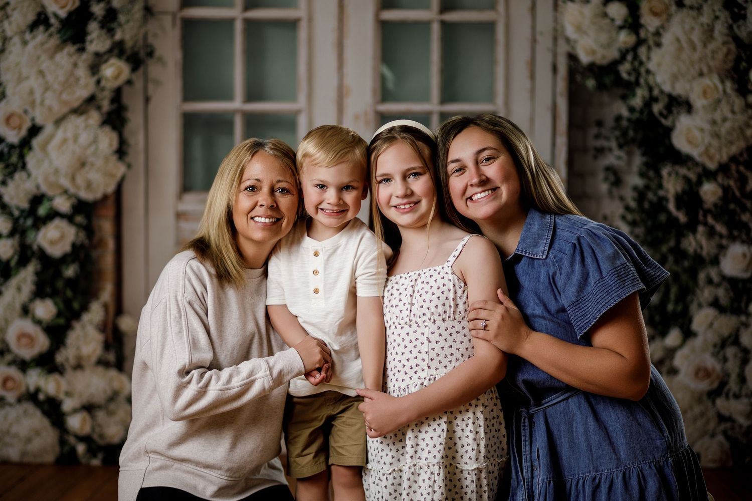A happy family of four smiles together in front of a floral backdrop.