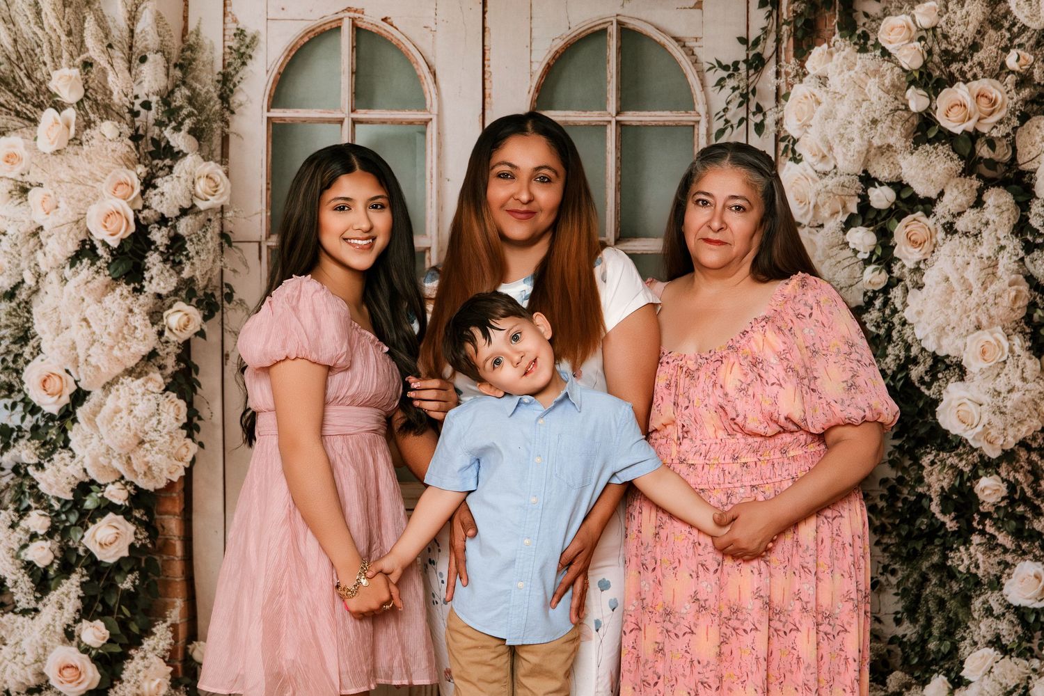 Family portrait of two women, a girl in pink dress, and a boy in blue shirt posing among white floral arrangements.