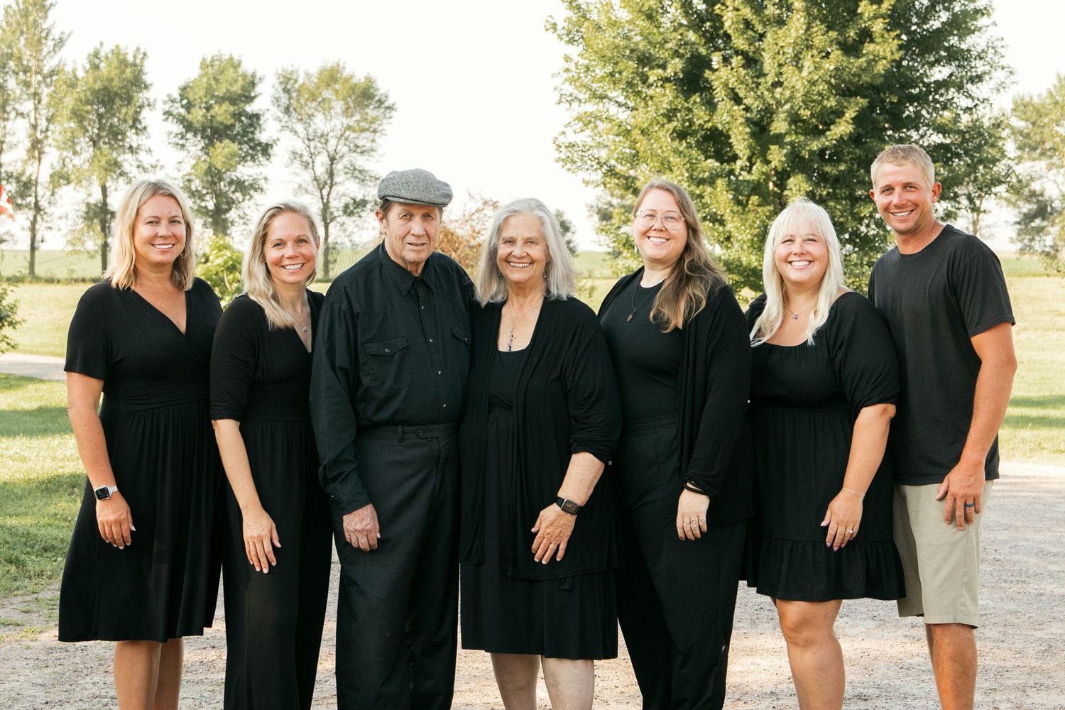 A group wearing coordinated black outfits poses together outdoors on a sunny day.