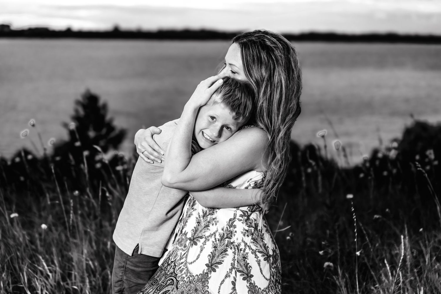 A sweet embrace between two people in a wildflower field at sunset captured in black and white photography.
