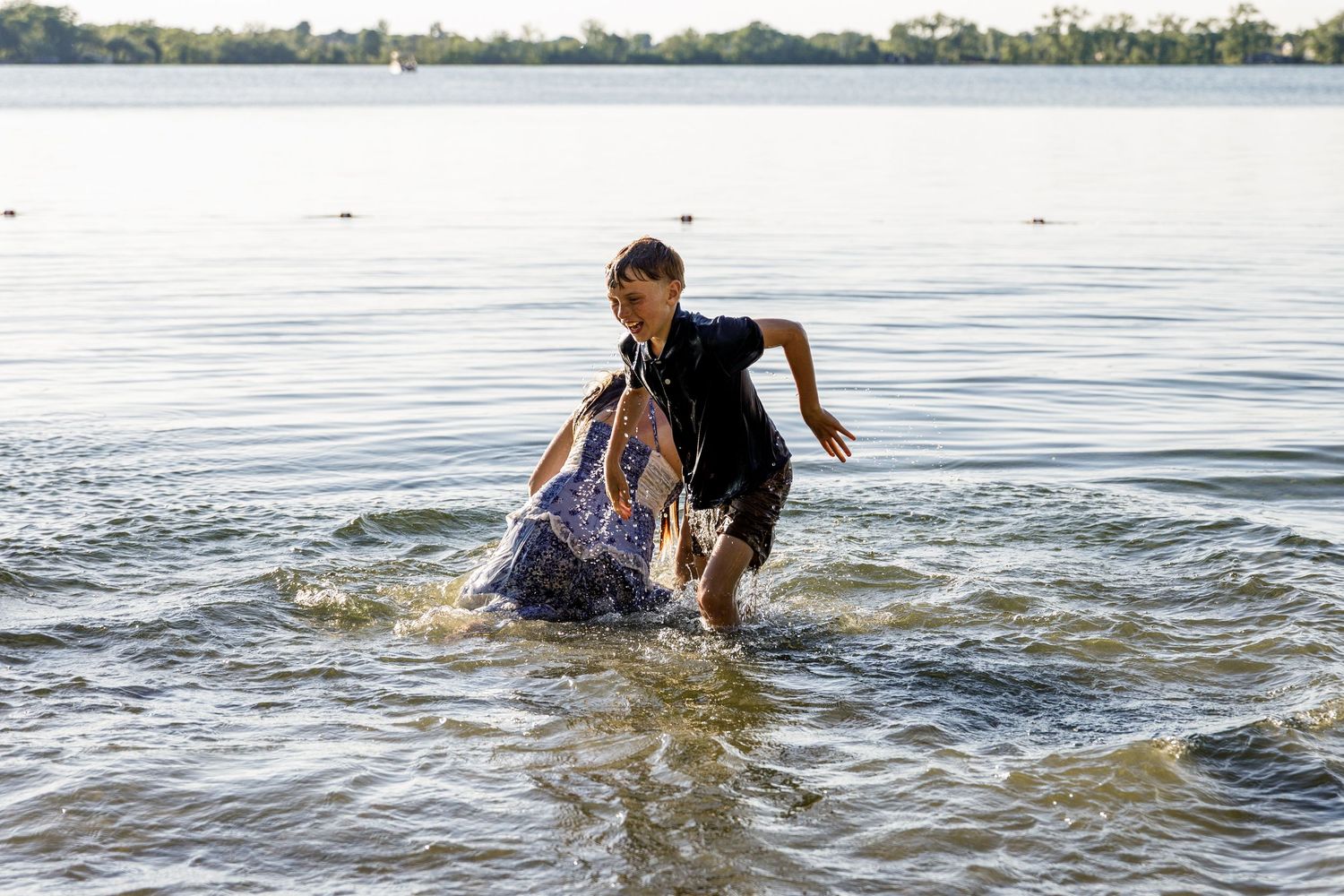 Young boy playfully pushing a woman into the lake water during a fun family photo session.