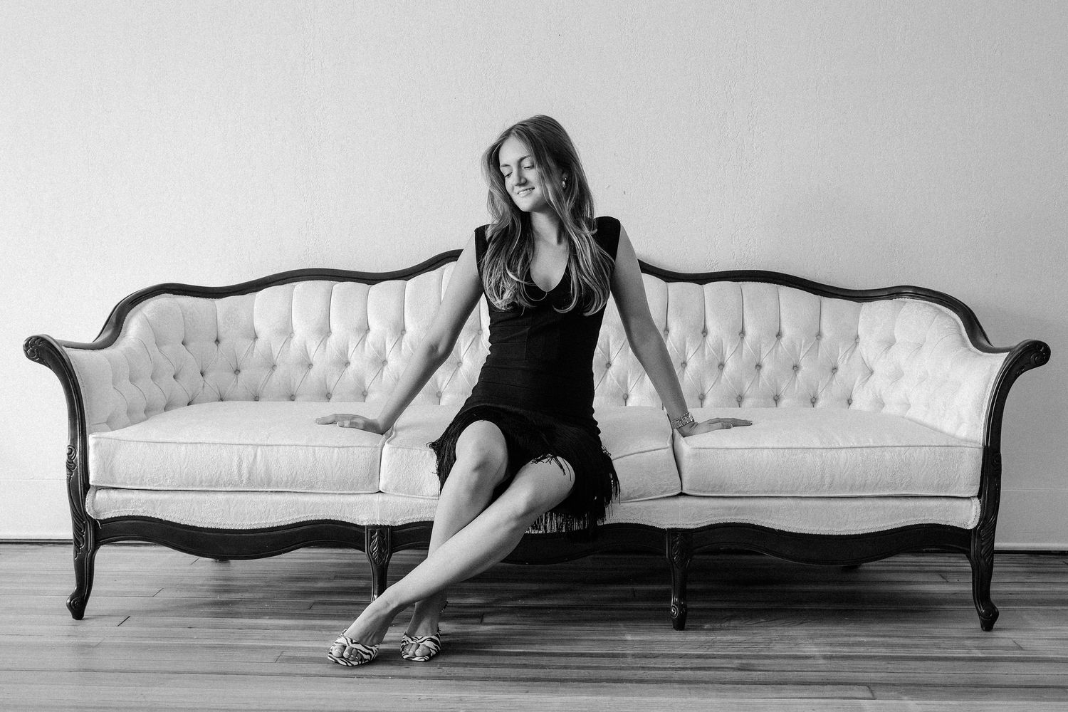 Black and white photo of woman in black dress sitting on elegant tufted white sofa.