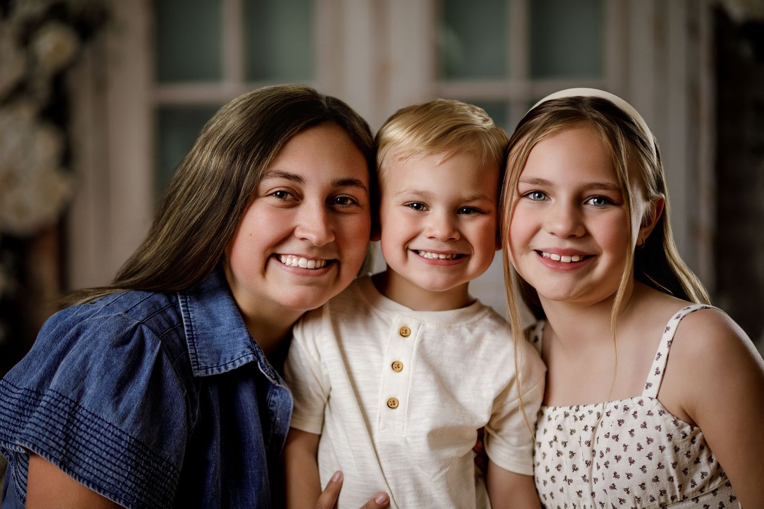 Three smiling children pose together for a portrait photo indoors.