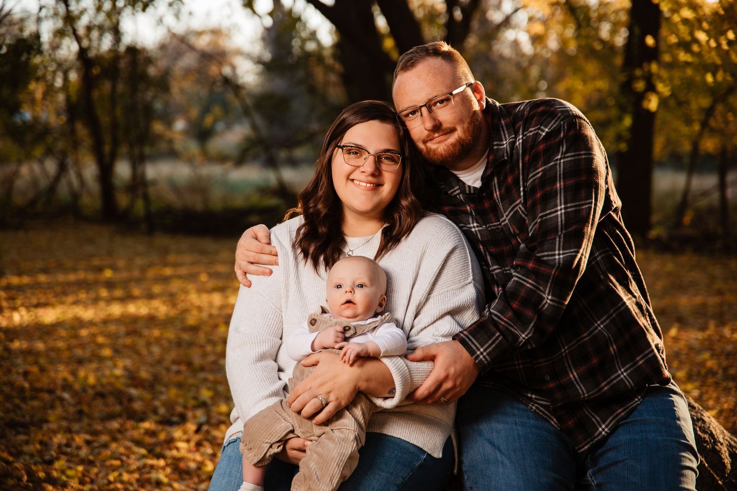 Family enjoying autumn sunset together in park with fallen leaves and warm golden light.