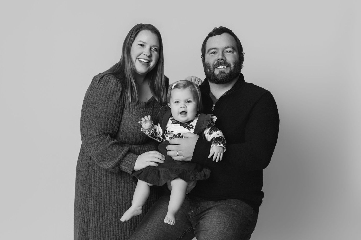 Black and white studio portrait of a family wearing cozy sweaters against neutral background.