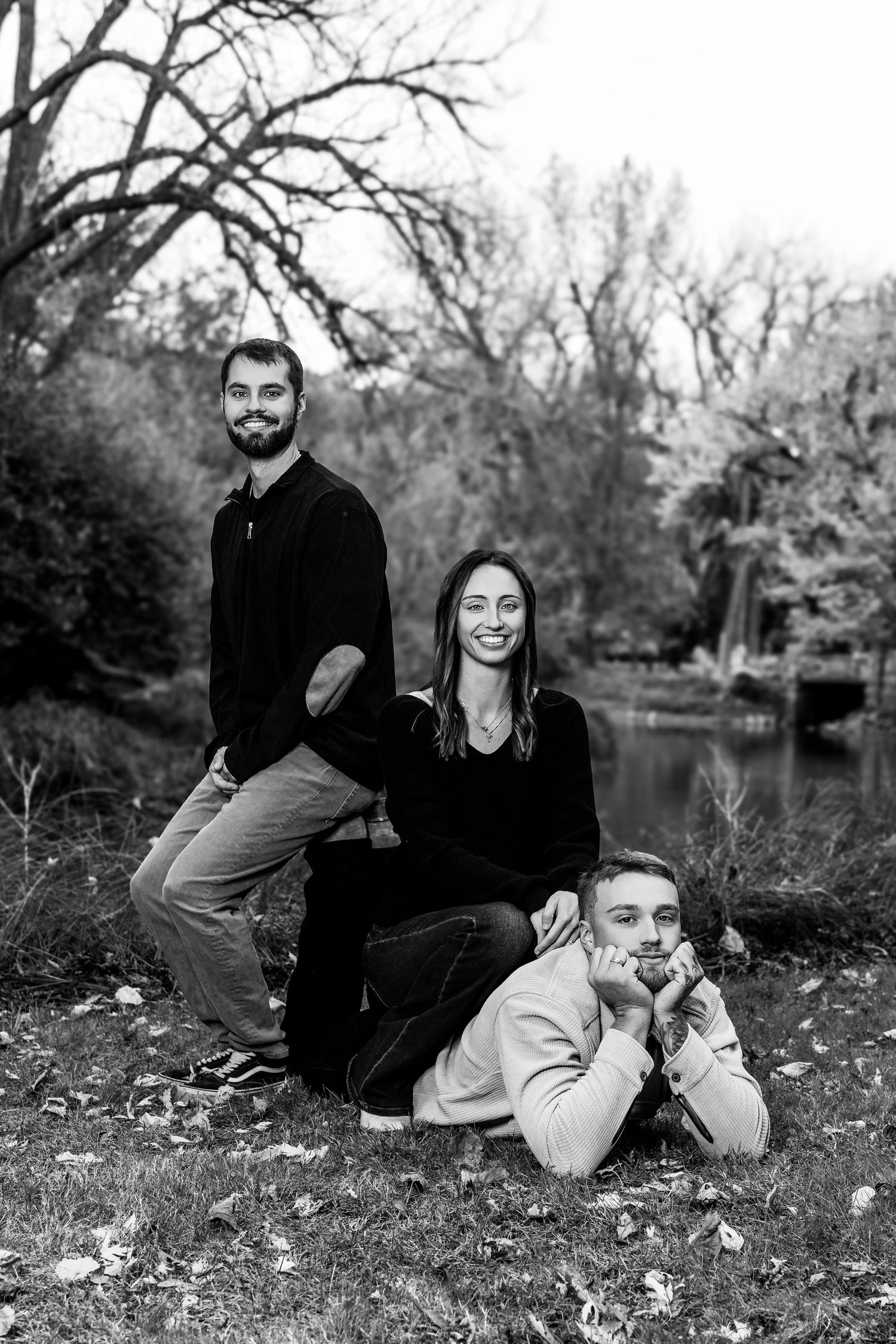 Black and white photo of a couple lounging on fallen leaves during an autumn photoshoot.