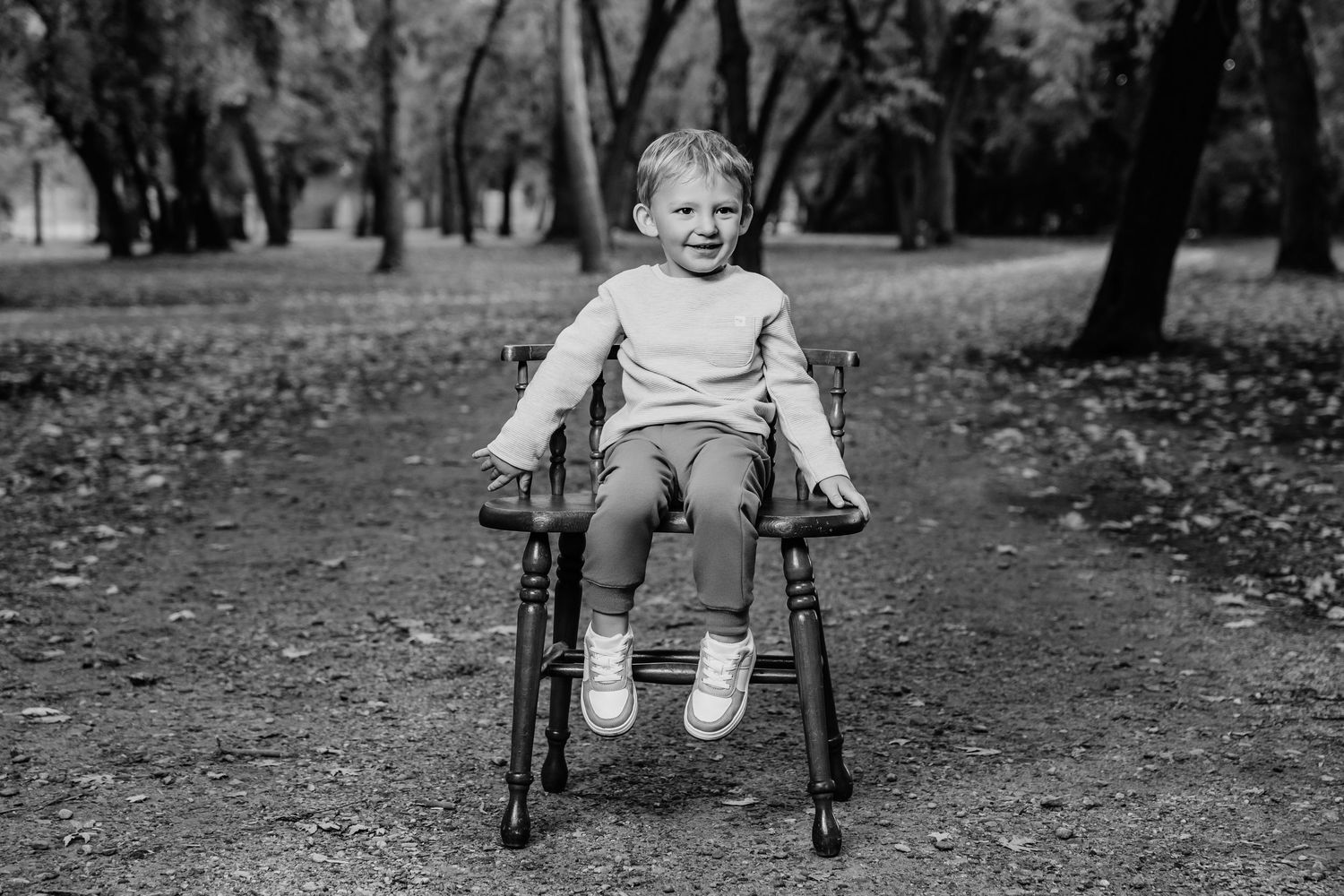 A young child sits in a wheelchair on a path surrounded by fallen leaves.