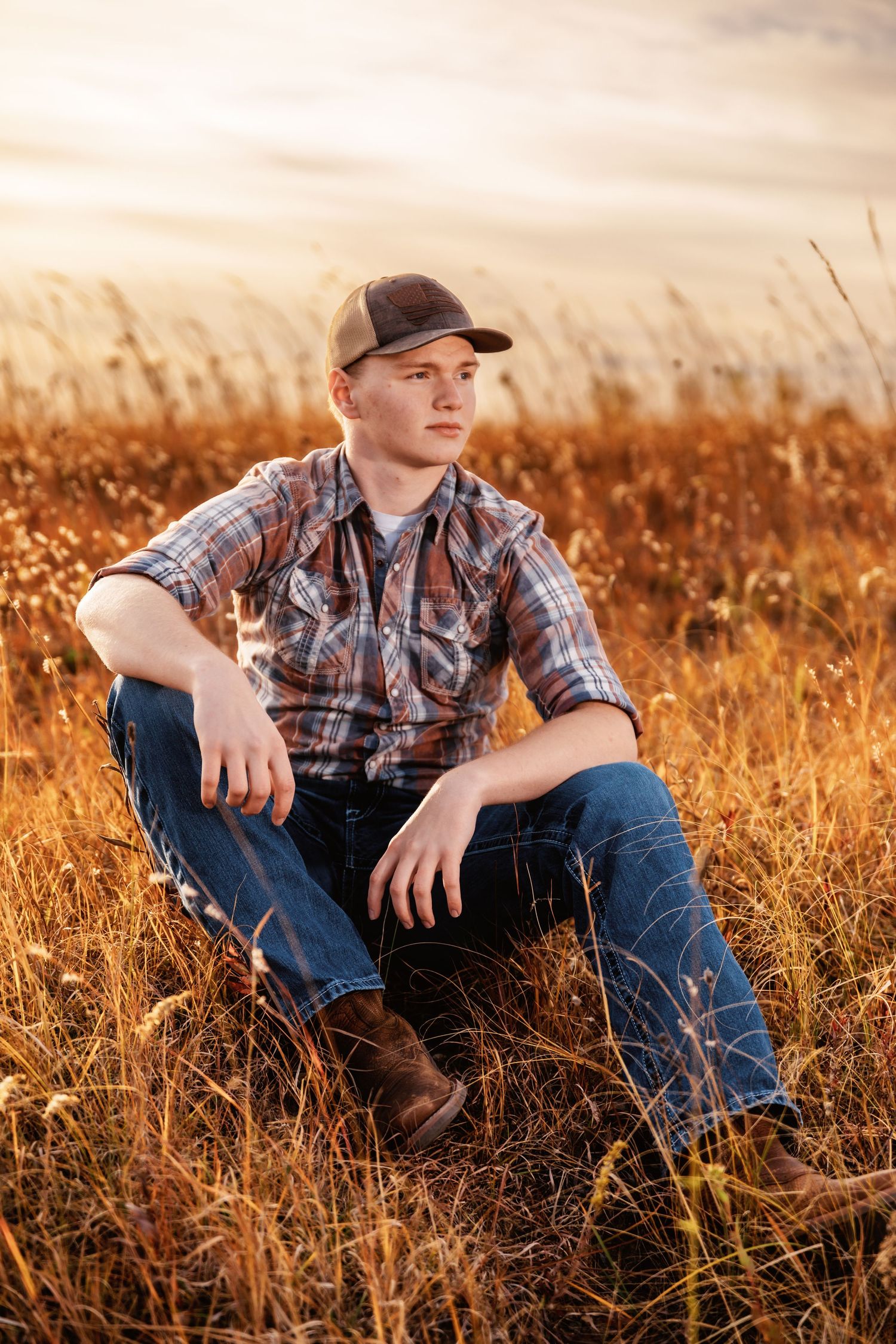 A person in plaid shirt and jeans sits in a golden field at sunset creating a rustic country portrait series.