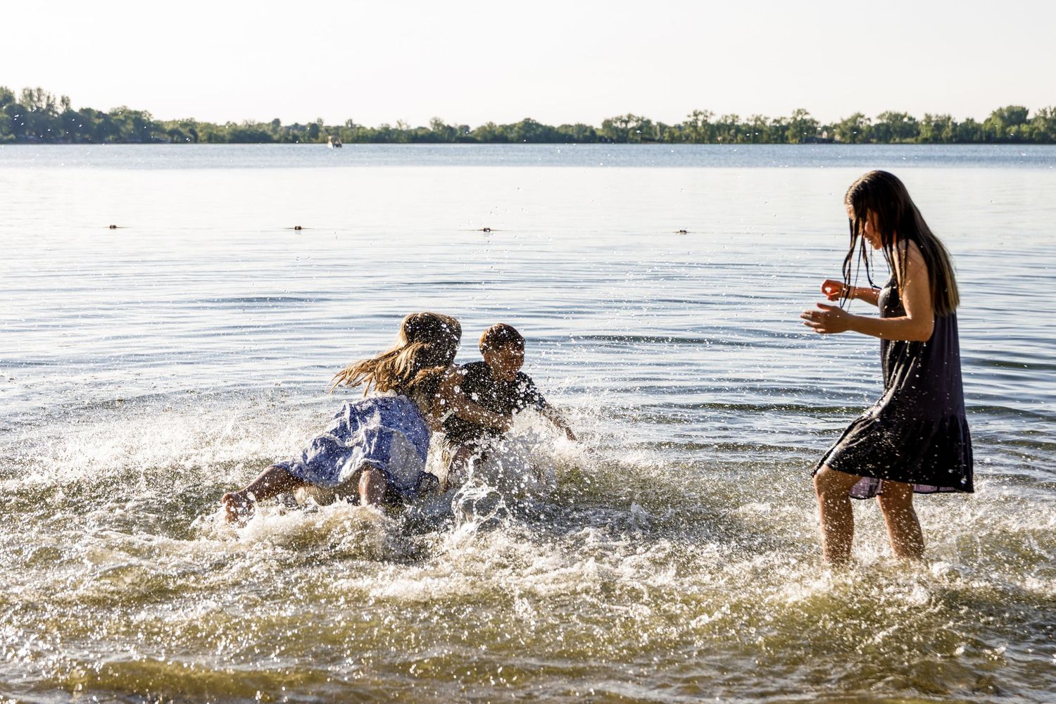Excited family members falling and splashing in lake water during a fun outdoor photo session.