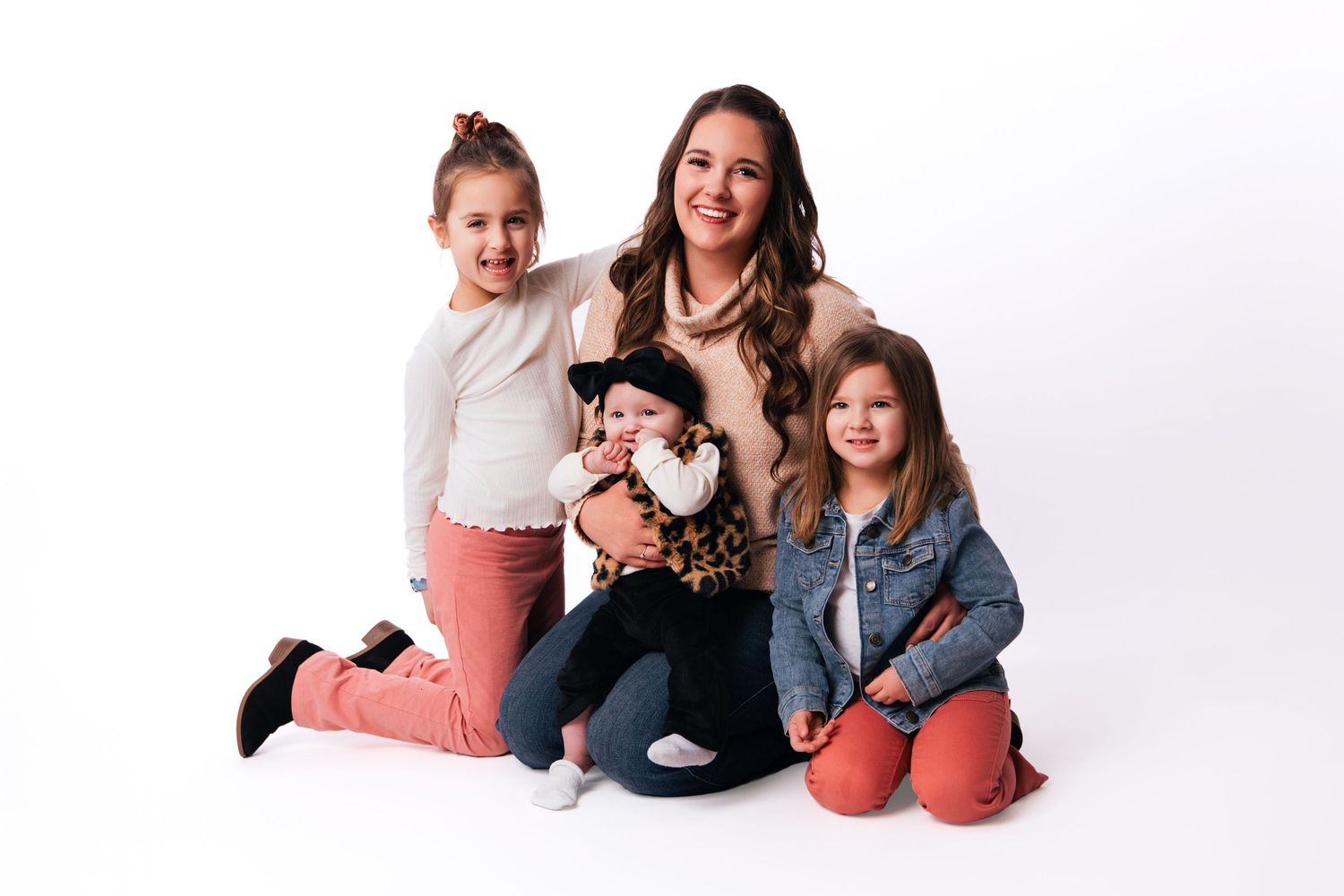 A woman poses with three young girls against a white background in a warm family portrait photo.