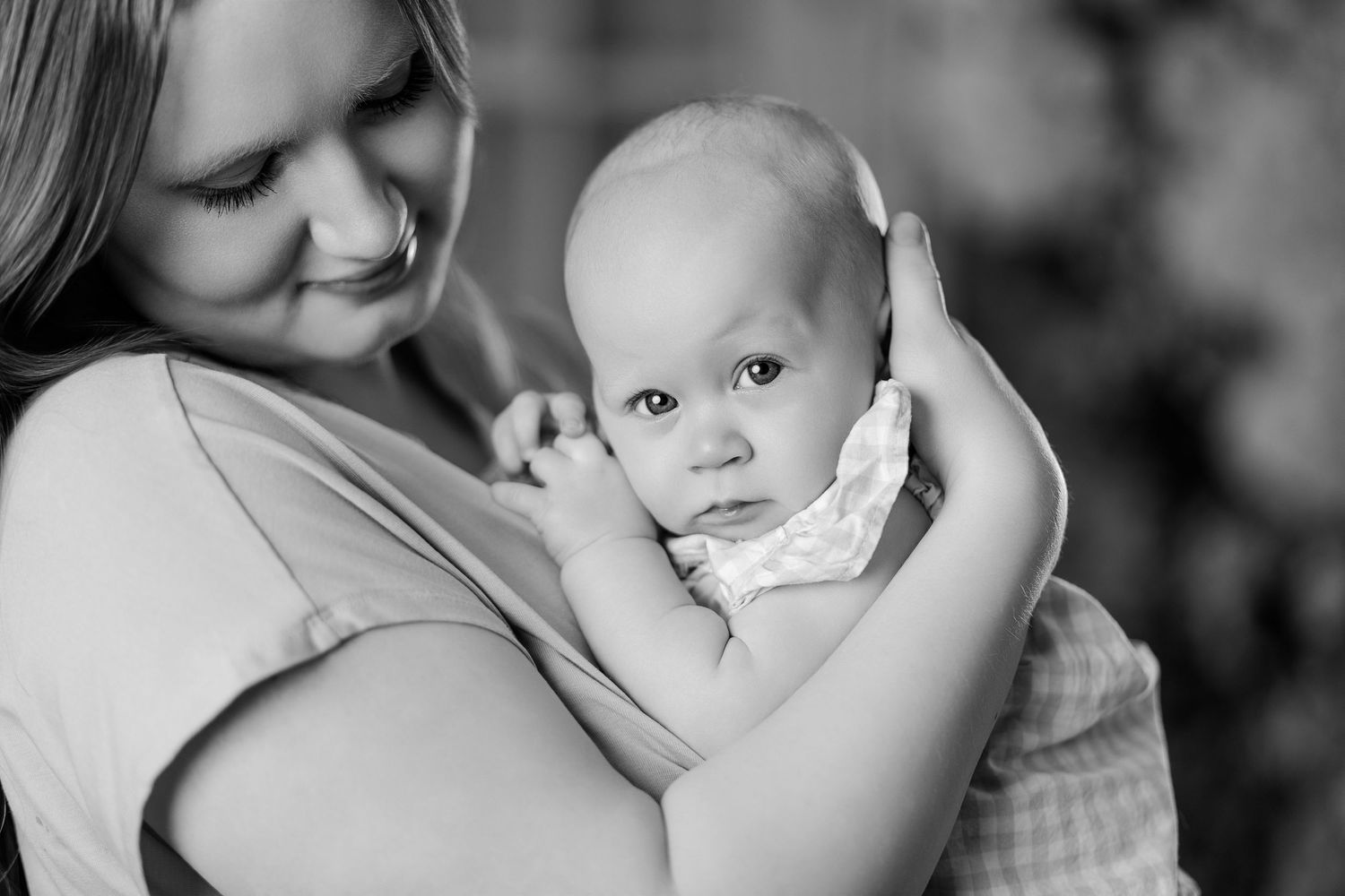 Black and white photo of a smiling mother tenderly holding her alert newborn baby close to her chest.