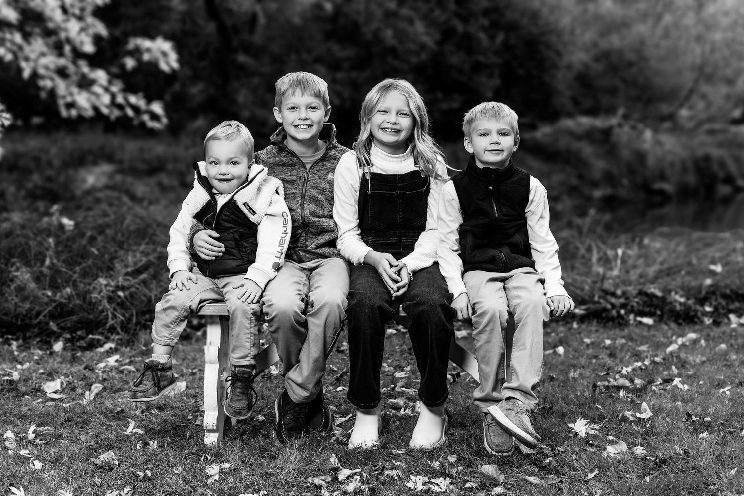 A black and white portrait of a family group sitting together on the ground during an outdoor photo session.