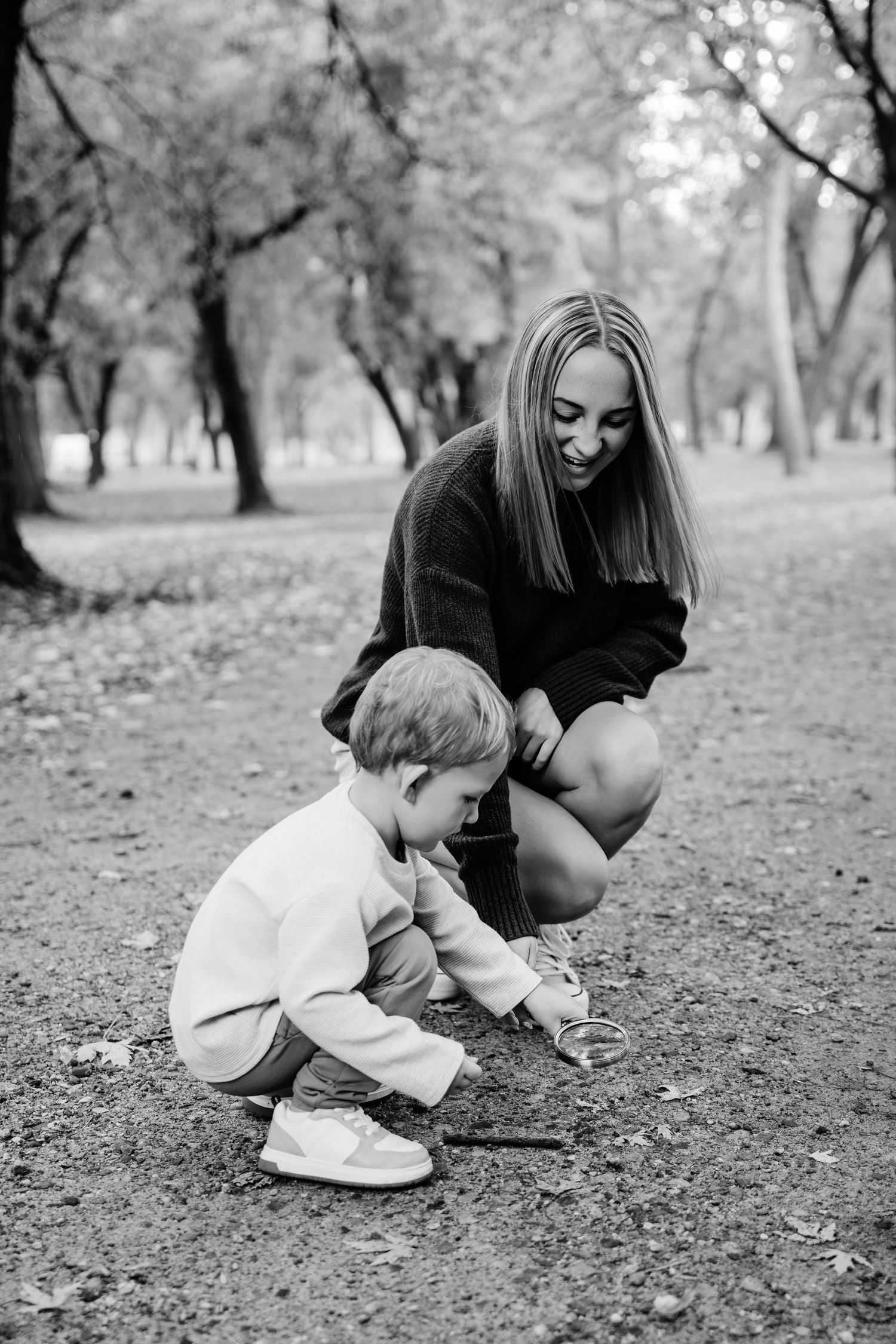 Black and white images of a parent and child exploring nature together on the ground in a park setting.