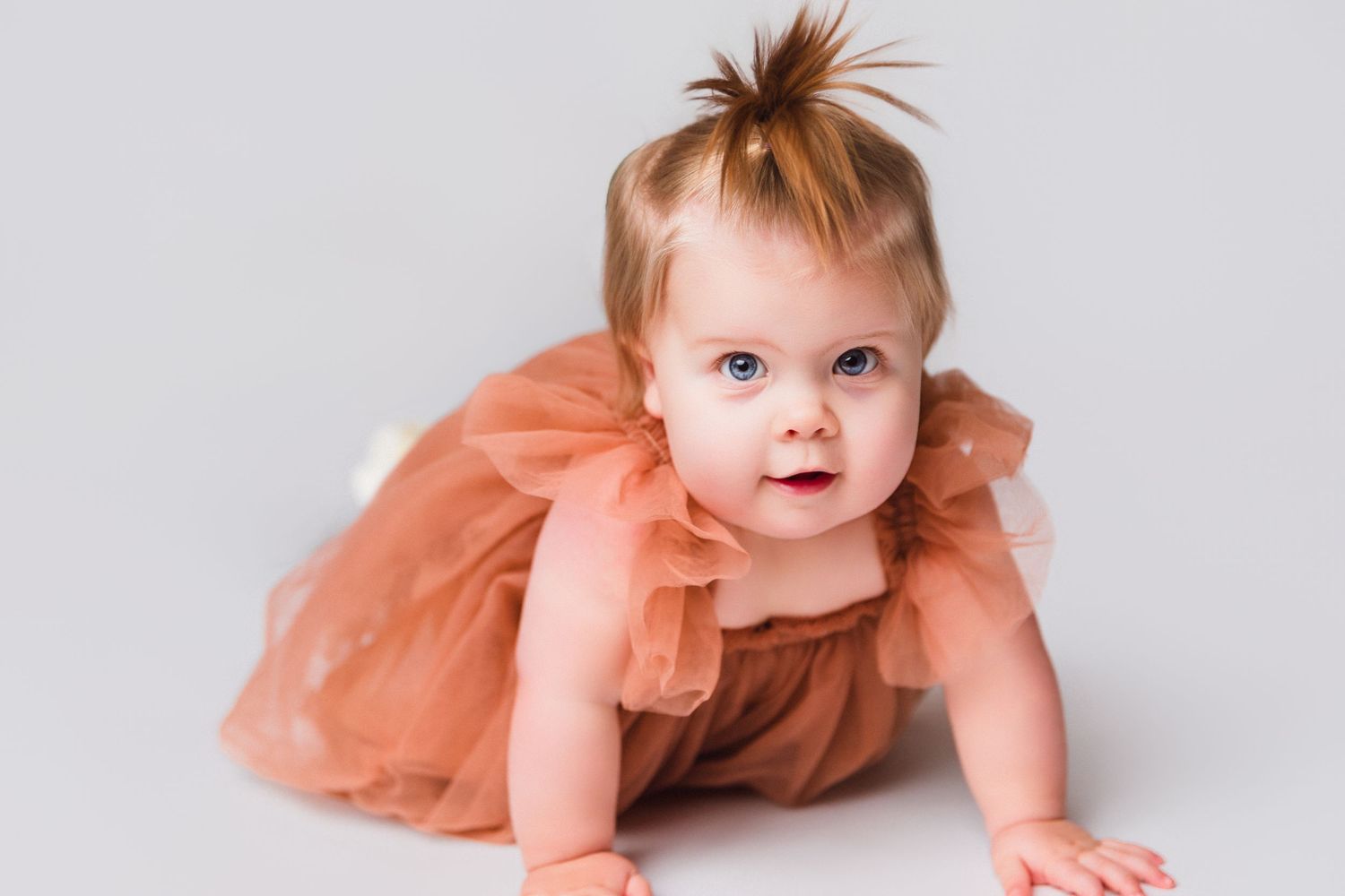 Baby in peach tulle dress crawling on white background.