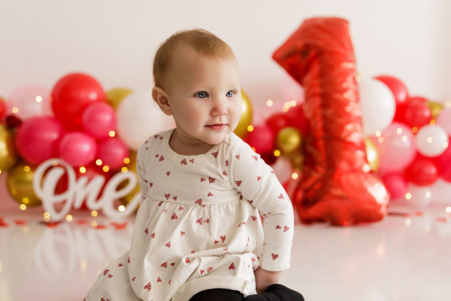 Valentine's Day themed photoshoot setup with red and pink decorations and balloons against a white backdrop.