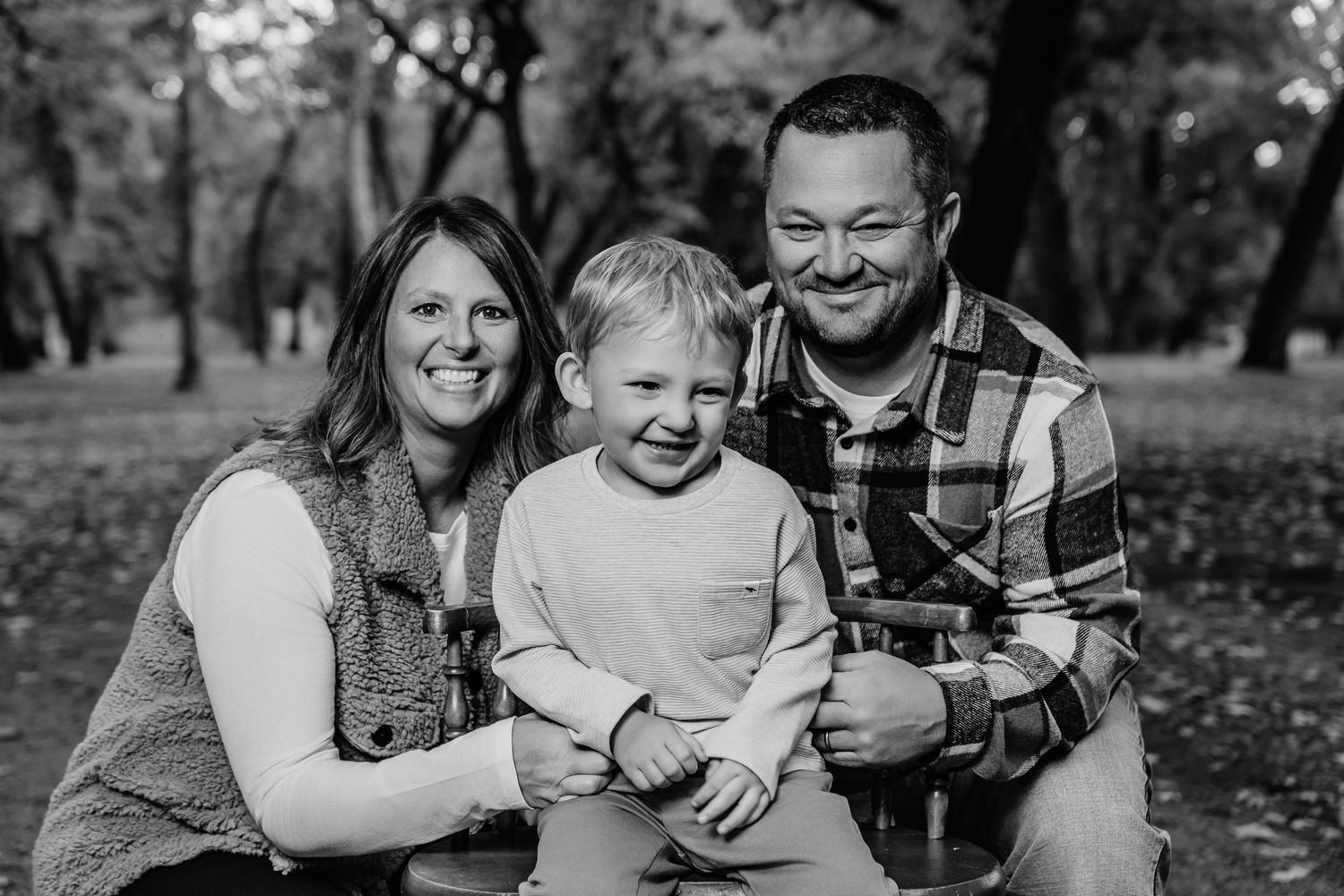 A family shares a candid black and white moment together in a wooded setting.