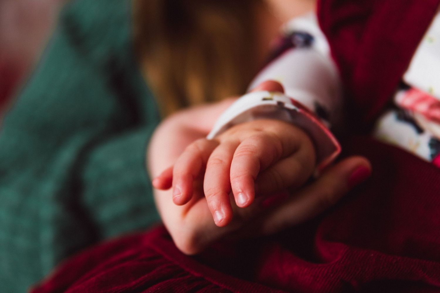 Close-up of small hands gently resting on burgundy fabric.