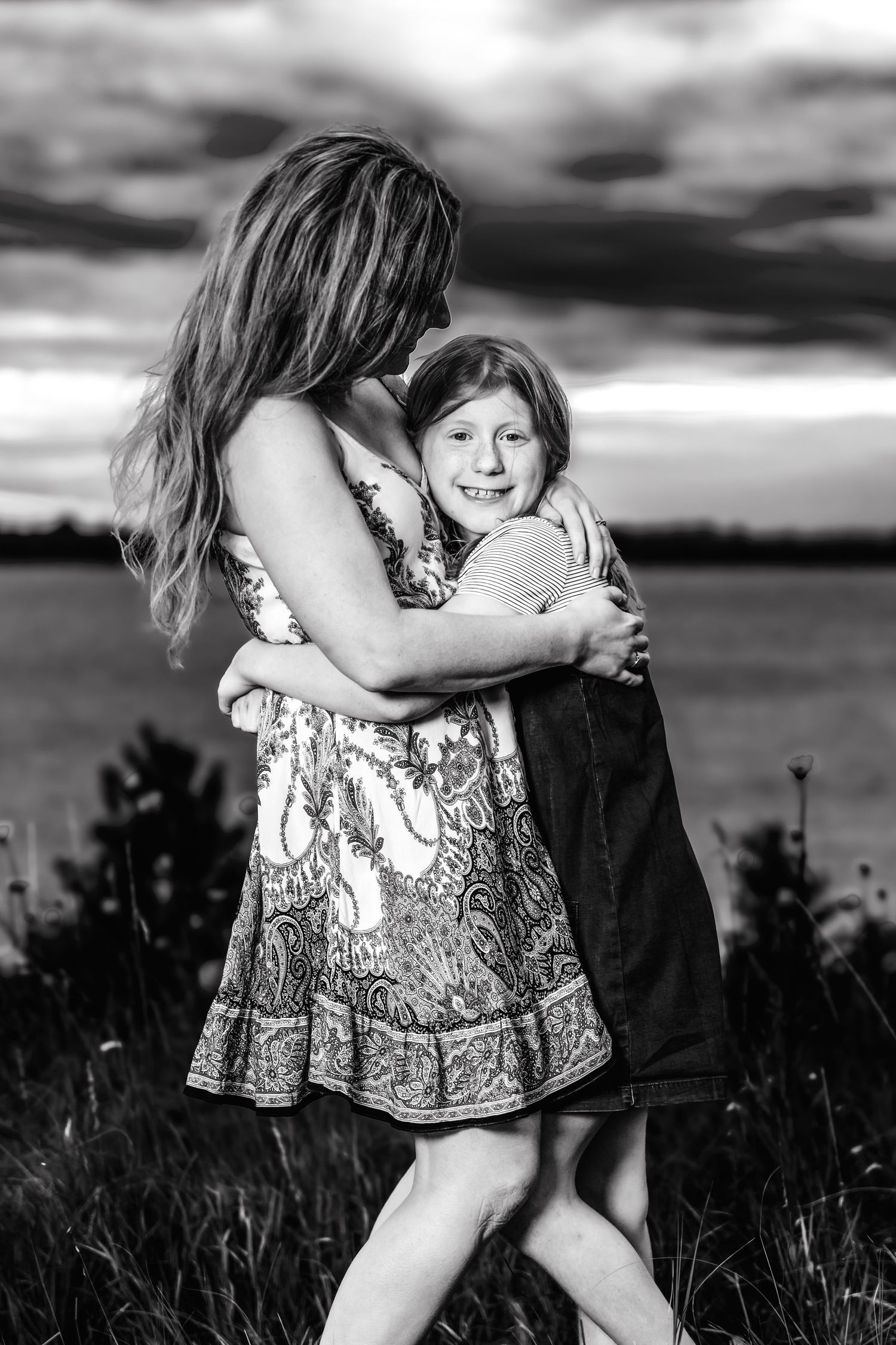 Black and white photo series of children playing in a field at sunset with dramatic clouds in the background.