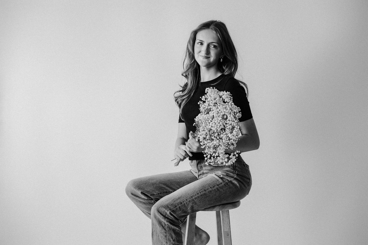 Black and white portrait of a young girl sitting on a stool holding a bouquet of flowers.