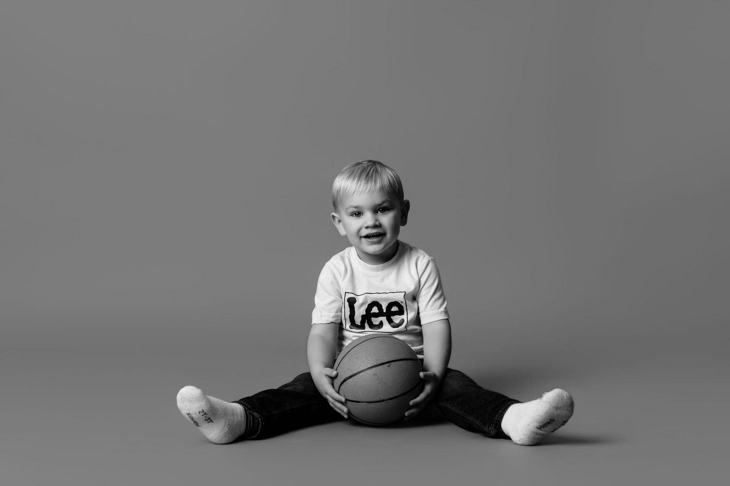 A child in athletic wear sits with legs spread on floor near a basketball.