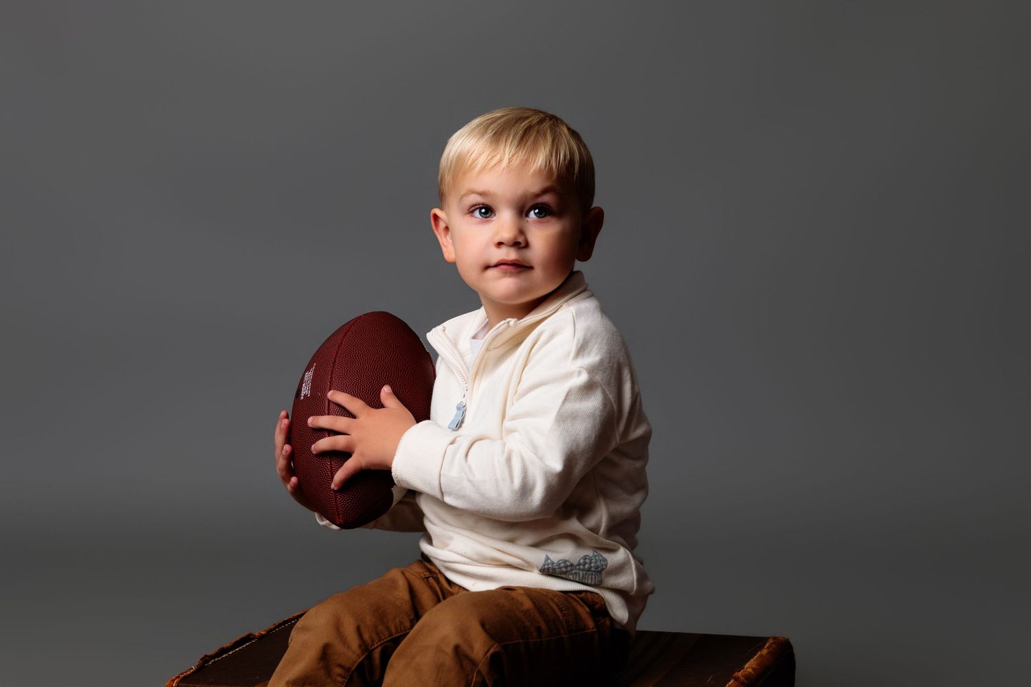 Studio portrait session with child in white sweater against dark grey background.