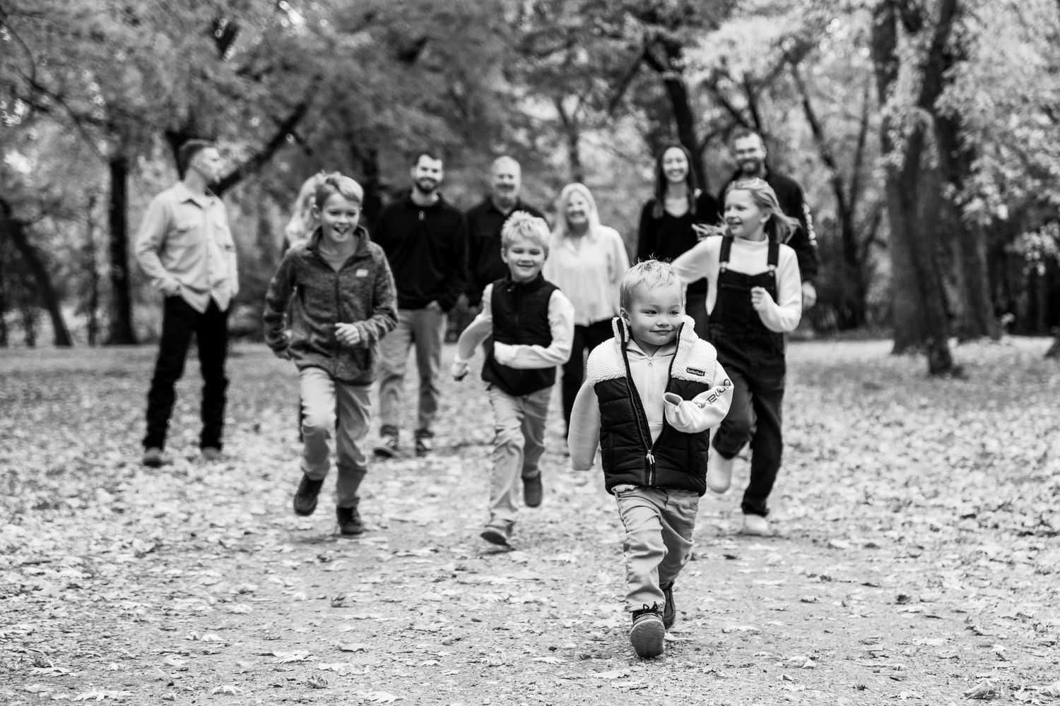 Black and white image of group walking through park covered in fallen leaves.