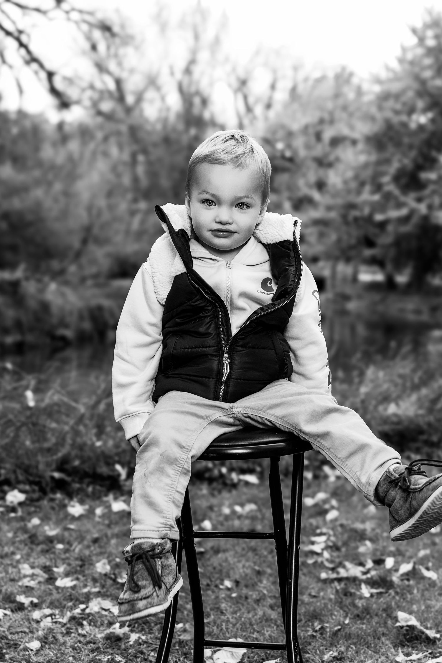 Black and white portraits of a child sitting on a wooden chair surrounded by fallen leaves.