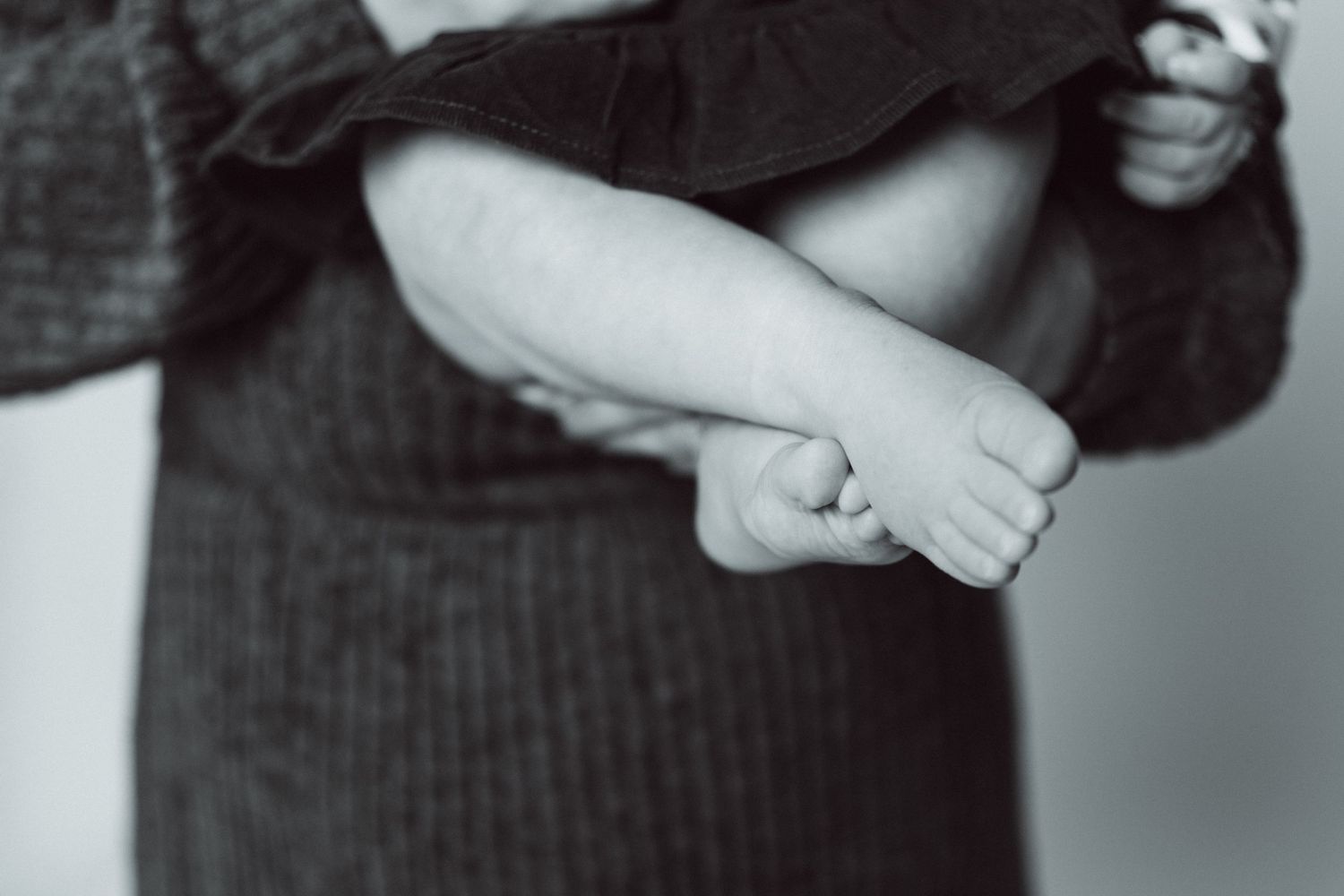 Black and white close-up of tiny baby feet against dark textured fabric.