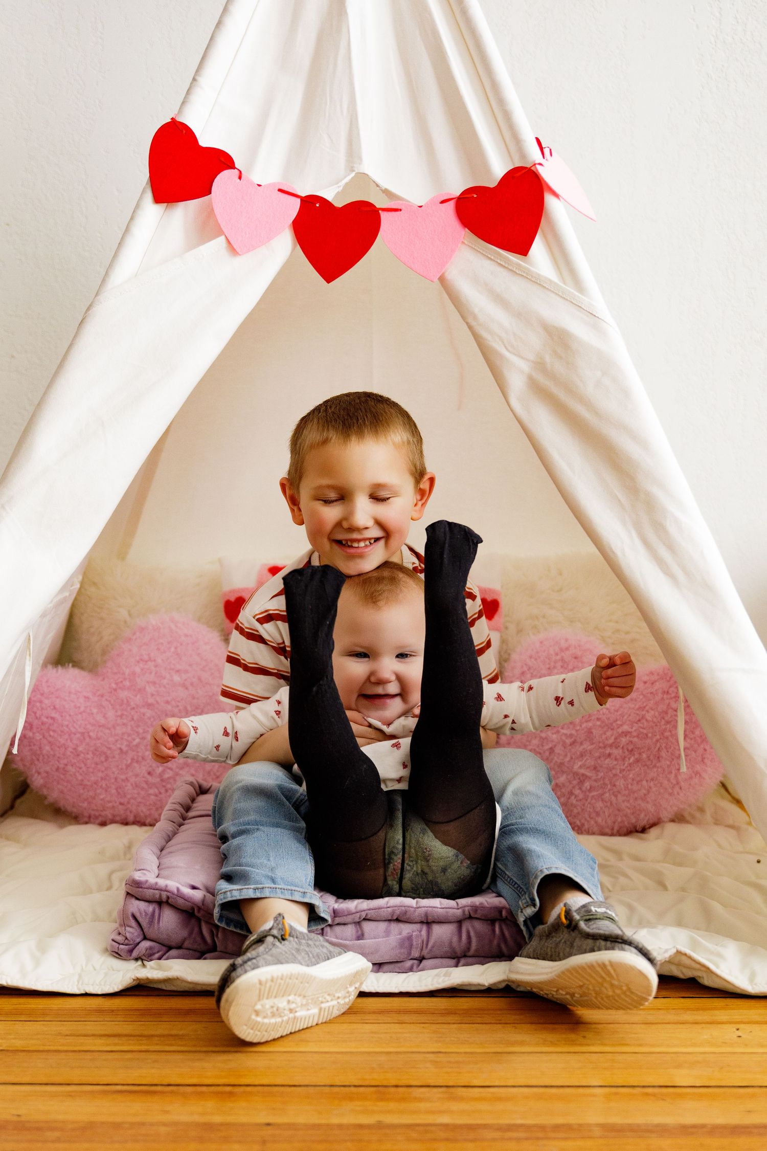 Child playing inside white teepee tent decorated with red heart garland.
