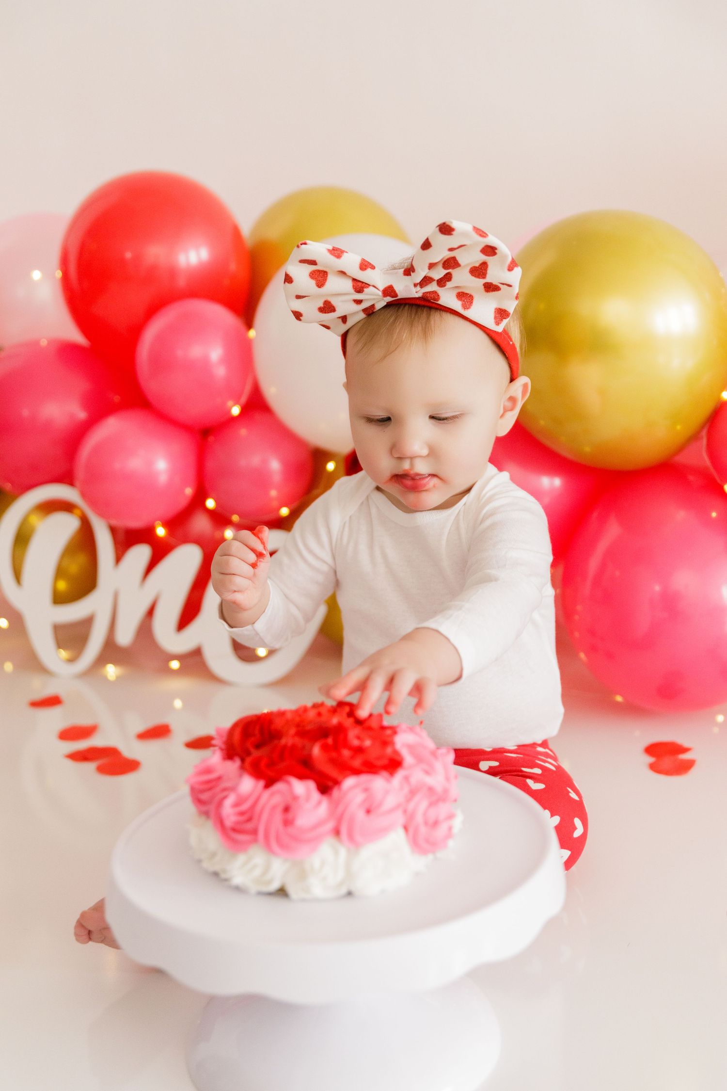 First birthday cake smash session with red and white decorations and balloon backdrop.
