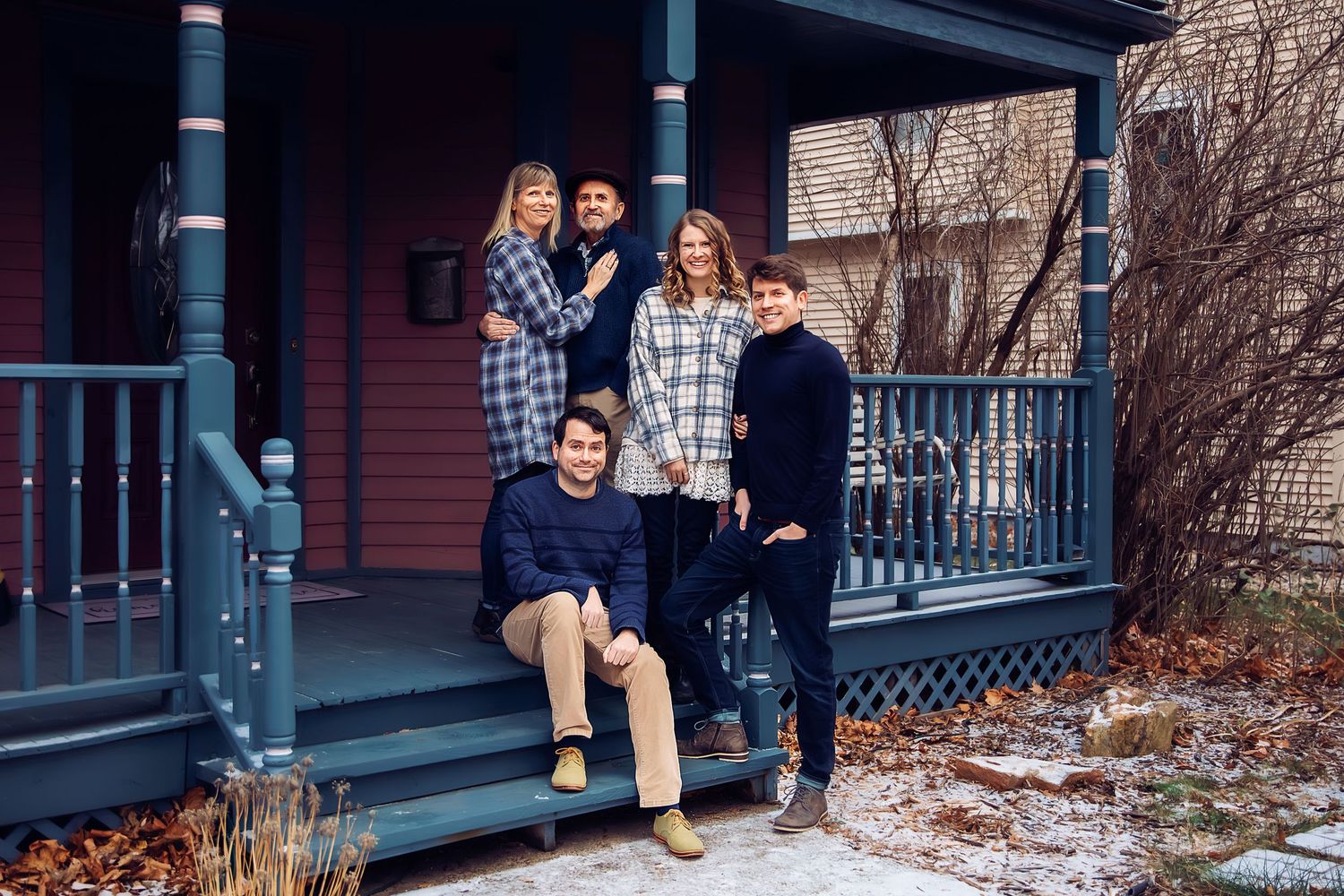 A family group poses together on a snow-covered front porch of a red house with ornate railings.