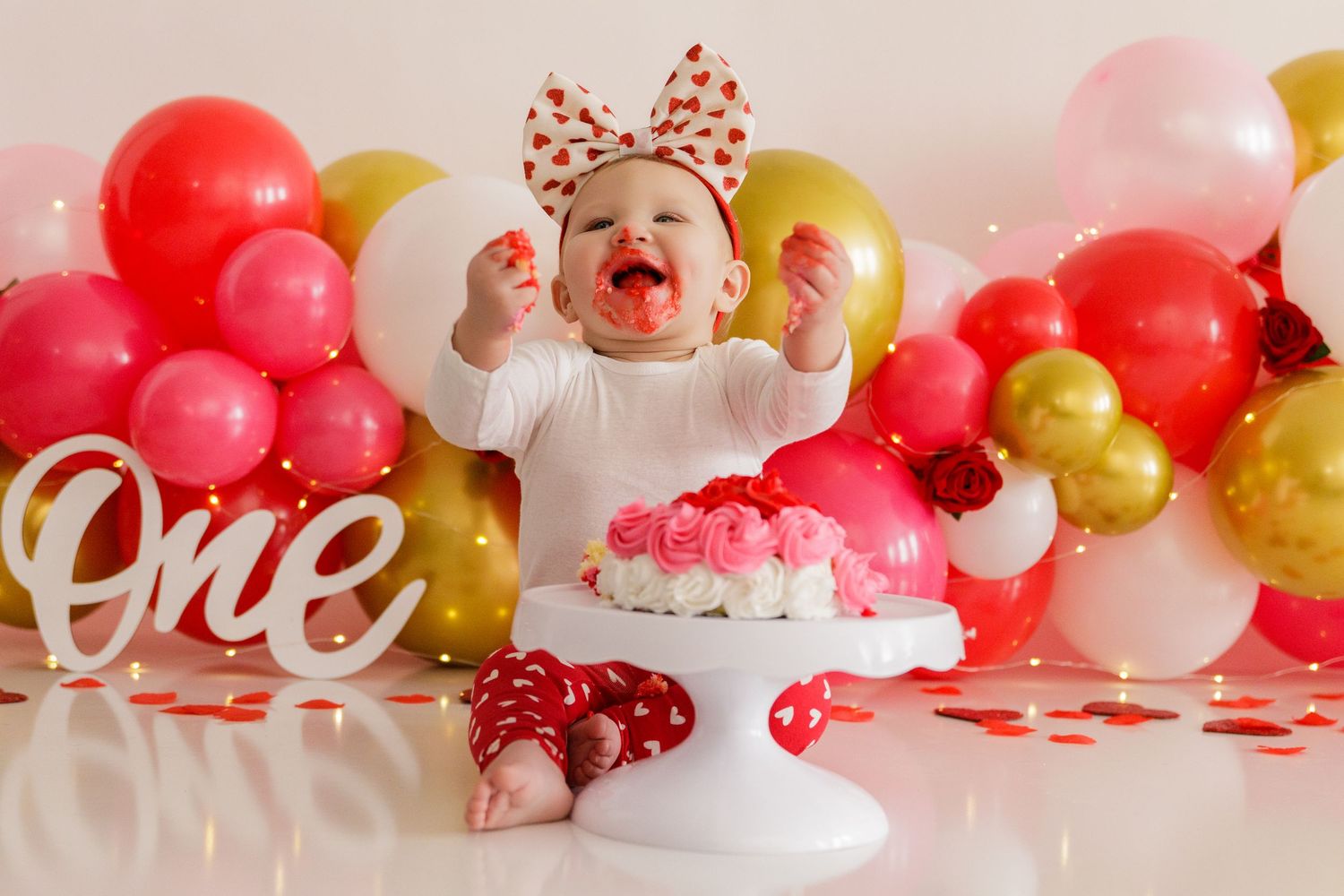 Pink and red Valentine's day setup with balloon garland and white decorative text.