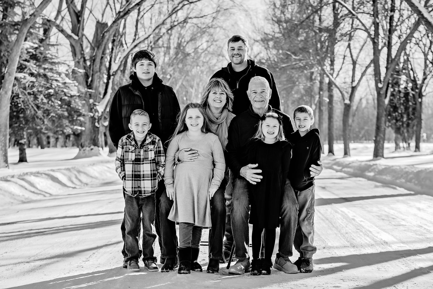 Black and white photo of people arranged together on a snowy winter path with bare trees.