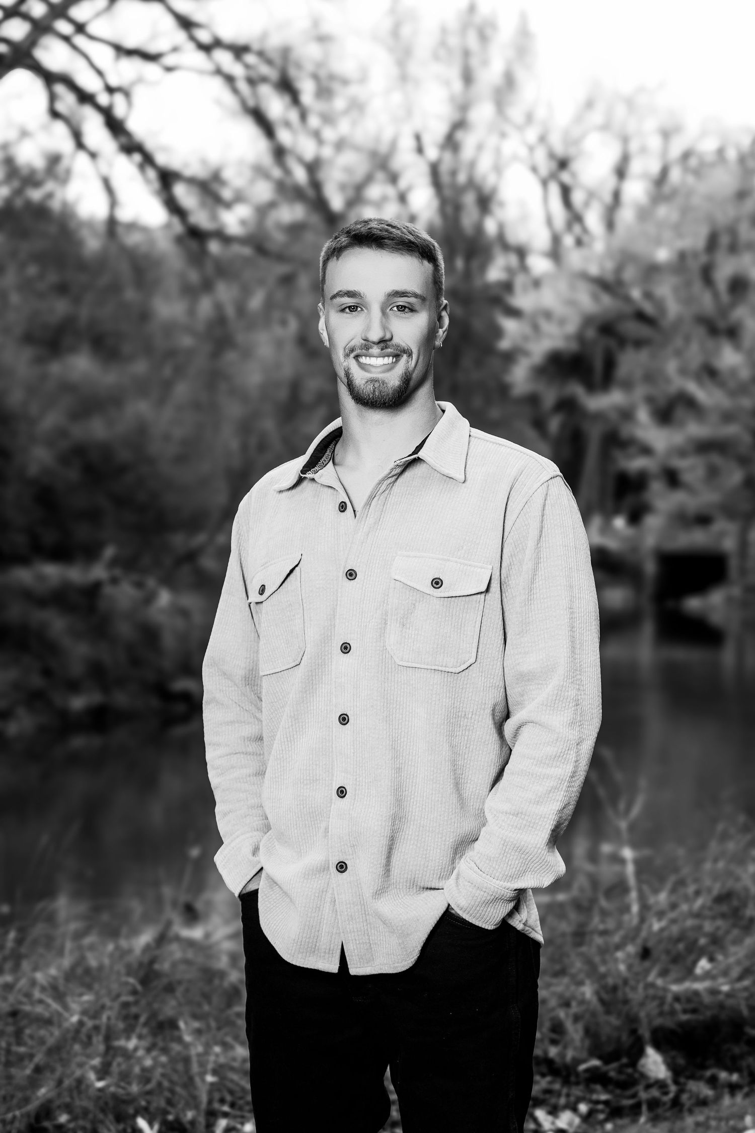 Portrait of person in light colored button-up shirt smiling by lake during fall season.