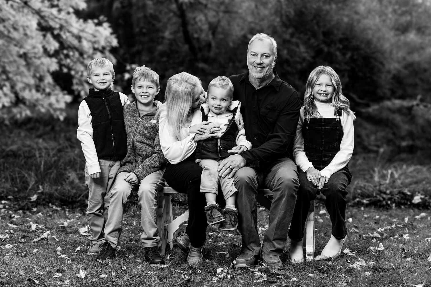 Black and white photo series showing a family enjoying playful moments together outdoors in a natural setting.