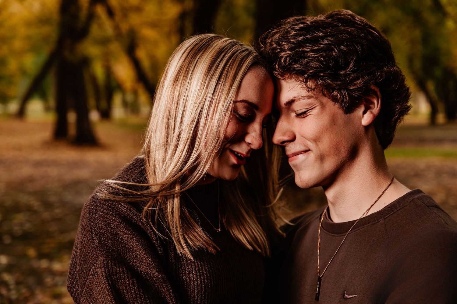 Romantic couple embracing in warm autumn sunlight with trees in background.
