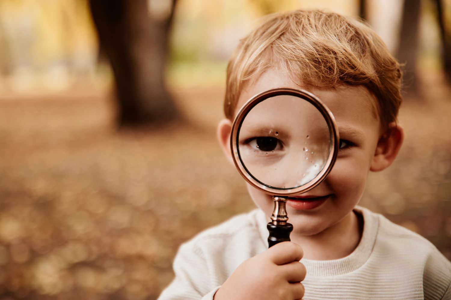 Close-up shot of young explorer with magnifying glass in autumn setting.
