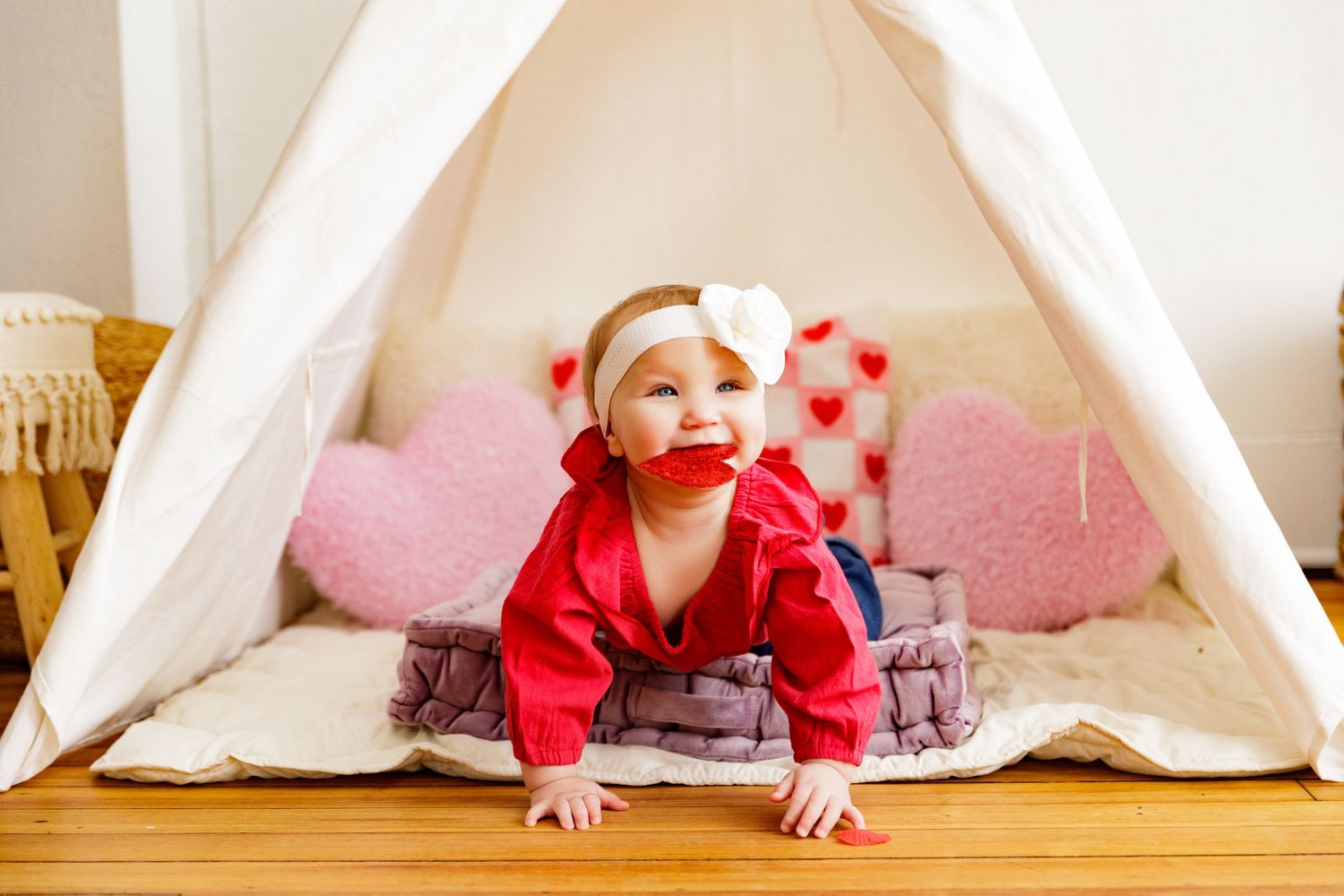 Small child crawling under white teepee tent with pink heart decorations.