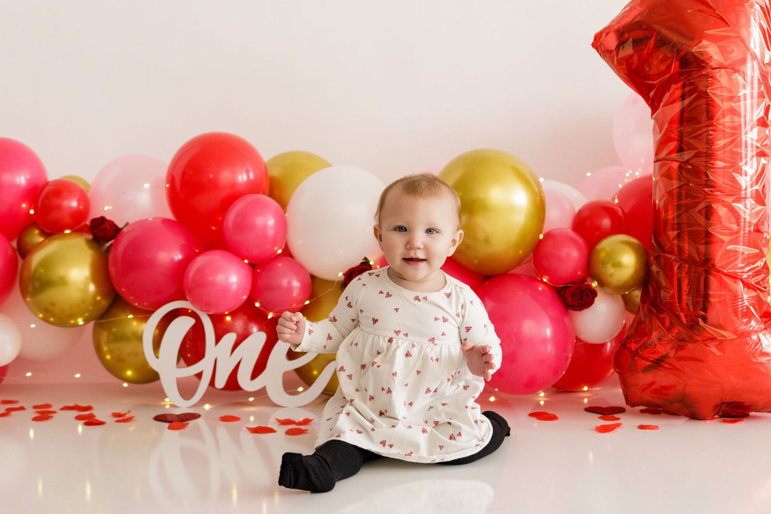 Colorful balloon garland with red and gold balloons creates celebratory backdrop for birthday photos.