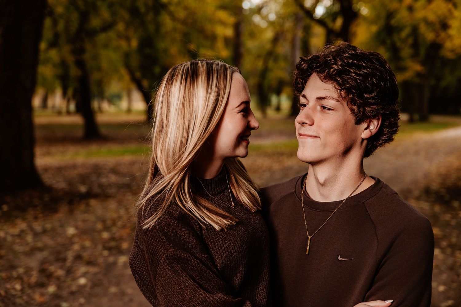 Two people share an intimate moment while standing in a sunlit autumn forest setting.