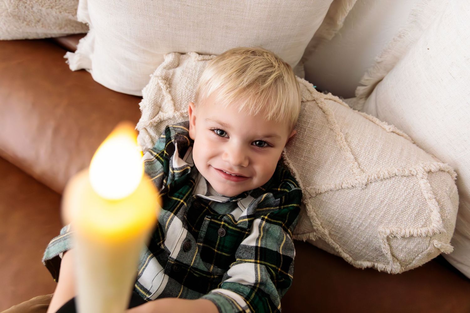 A child in plaid pajamas lies on white bedding near a glowing candle.
