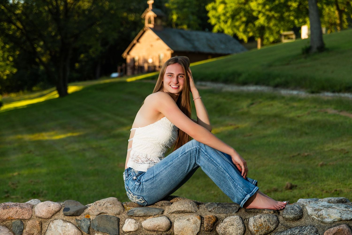Someone sits casually on a stone wall at sunset with a rustic chapel visible in the background.