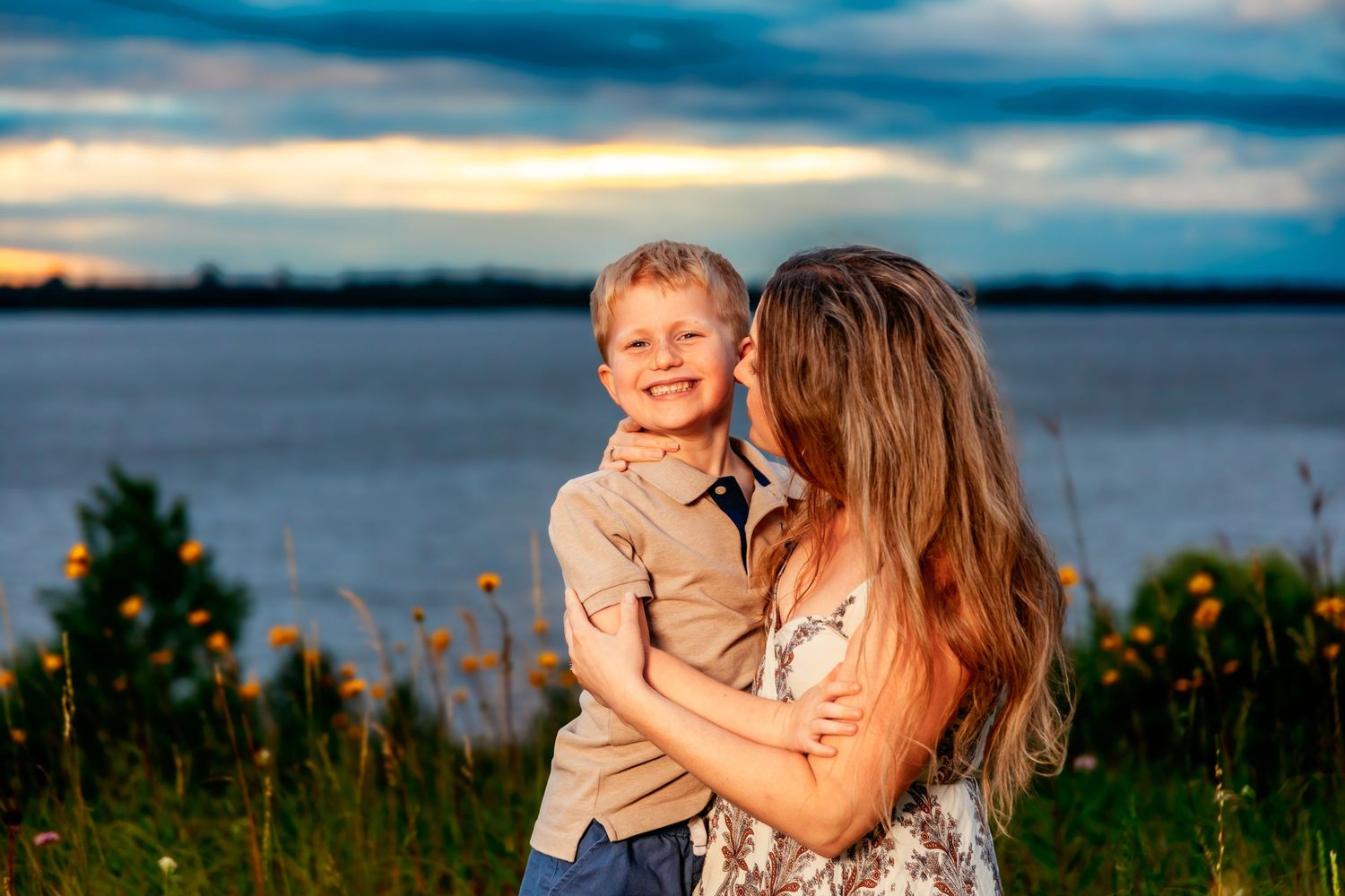 Two people share a joyful moment together by a lakeside during golden hour with wildflowers in the foreground.