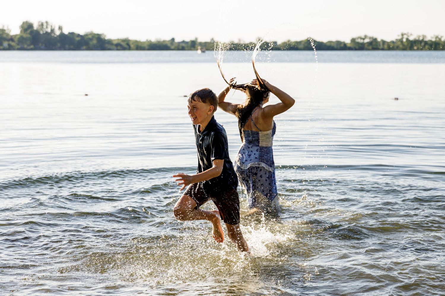 Two children laughing and splashing through shallow lake water on a sunny day.