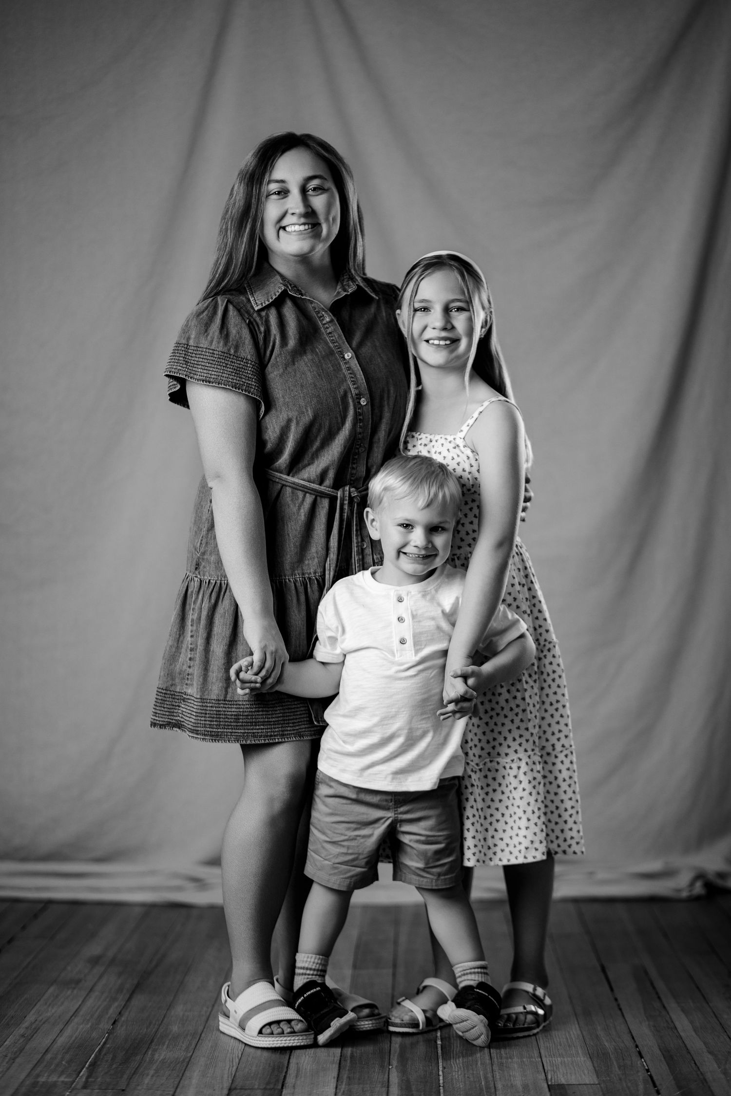 Black and white portrait of older sister and younger brother posing together in a photo studio.