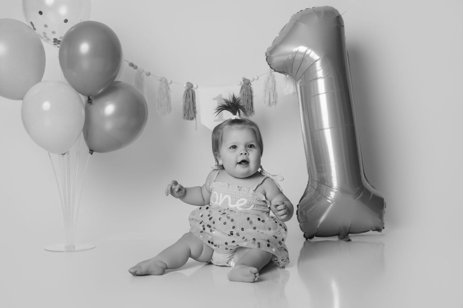 Baby poses with silver and white balloons during milestone photo session.