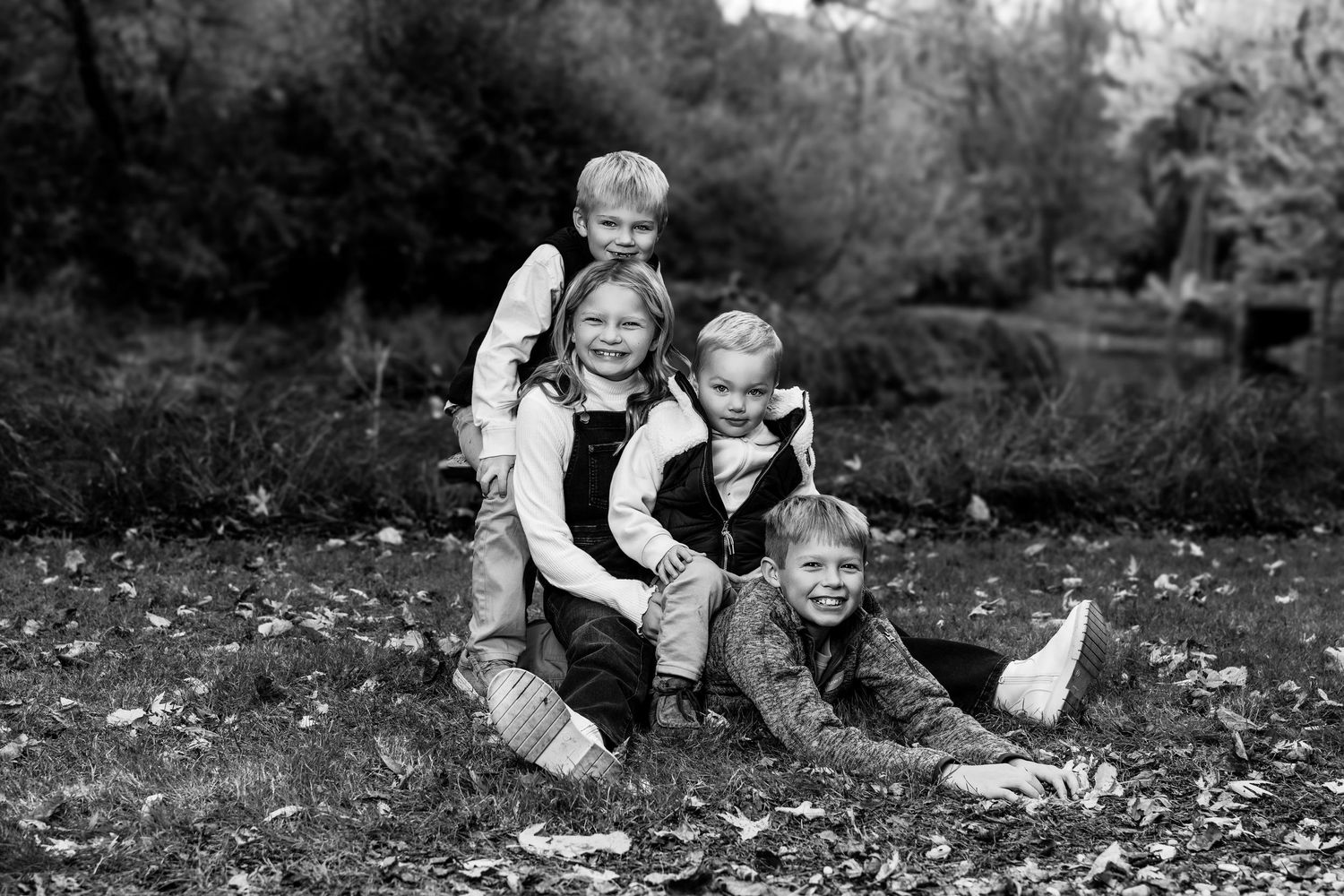 Black and white photo of family playing together on ground covered with fallen leaves.