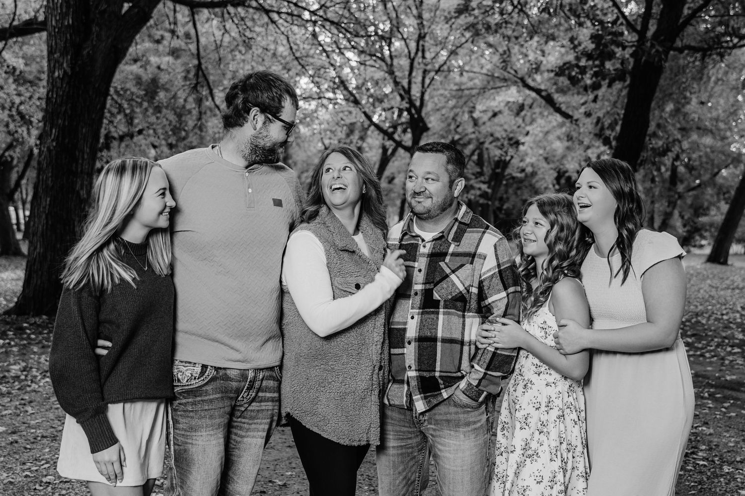 A group of people laughing and enjoying a casual outdoor gathering in a park setting.