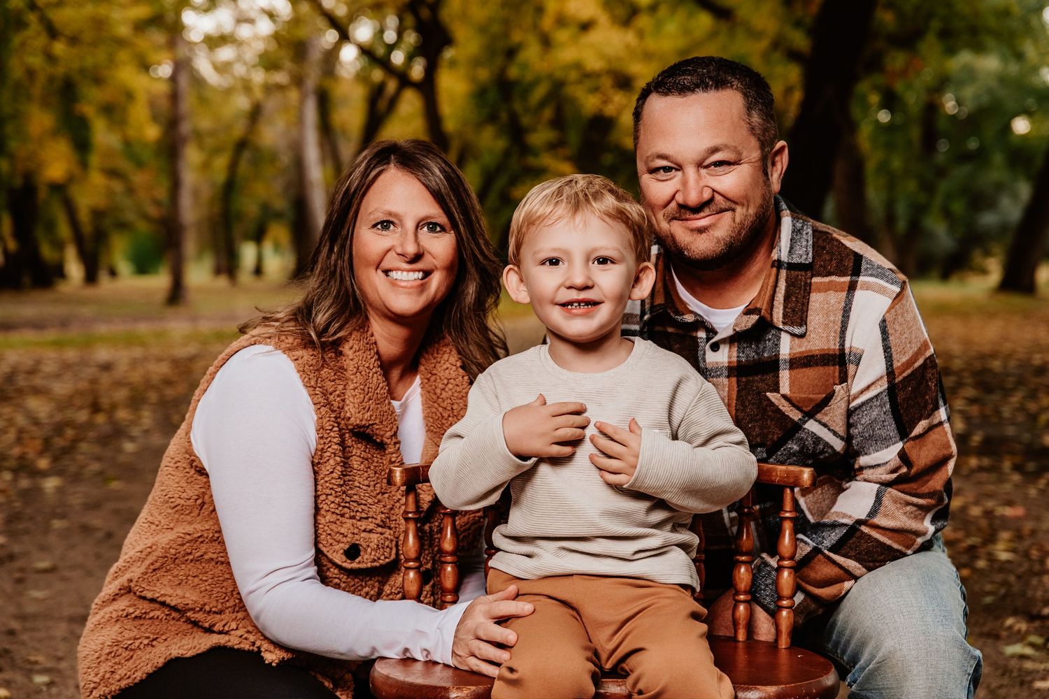 Family portrait session in a park with warm autumn colors and fallen leaves.