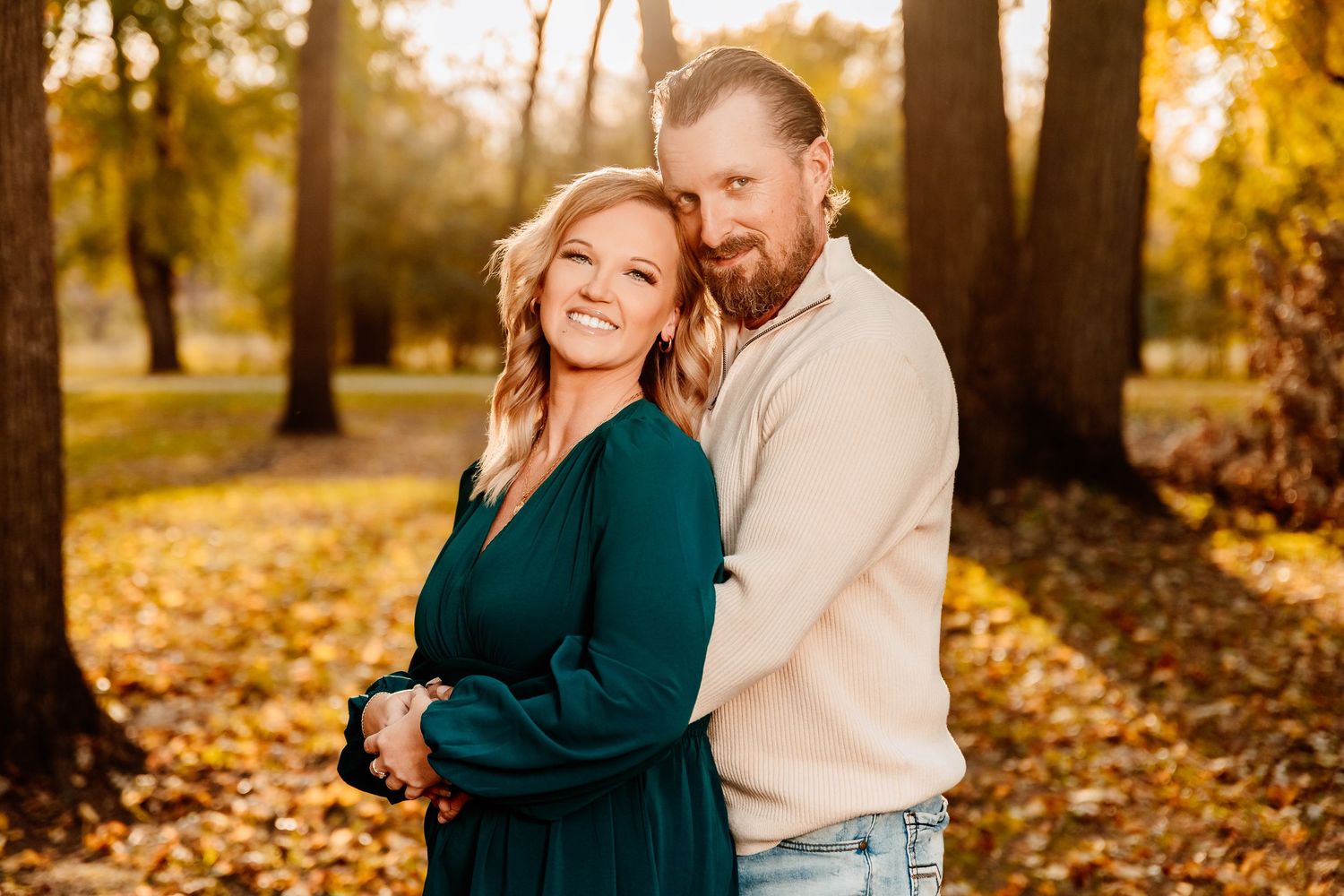 A couple embraces in a park during autumn with golden leaves and sunlight creating a warm, romantic atmosphere.